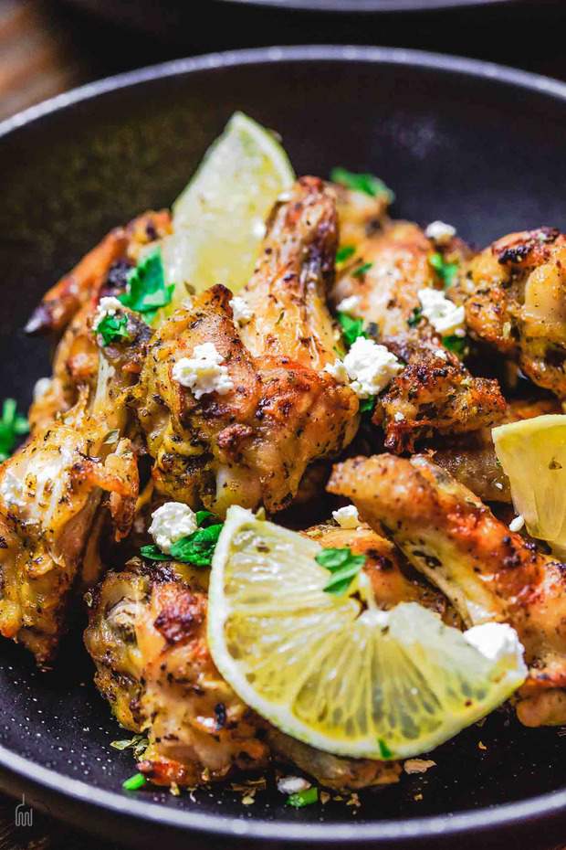 Easy Baked Chicken Wings Recipe; prepared Greek-style with garlic, olive oil, lemon juice and oregano. Finished with a little feta cheese and fresh parsley and served with a classic Greek Tzatziki sauce.