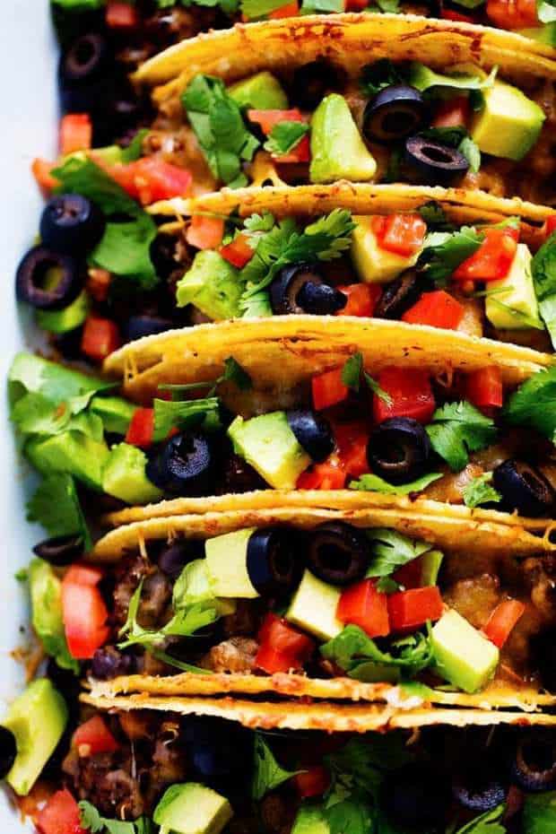 Beefy Baked Tacos are ready for the dinner table in under 30 minutes!  They are layered with refried beans, a black bean taco seasoned ground beef and topped with melty cheese.   Load them up with all of your favorite toppings and your family will devour them