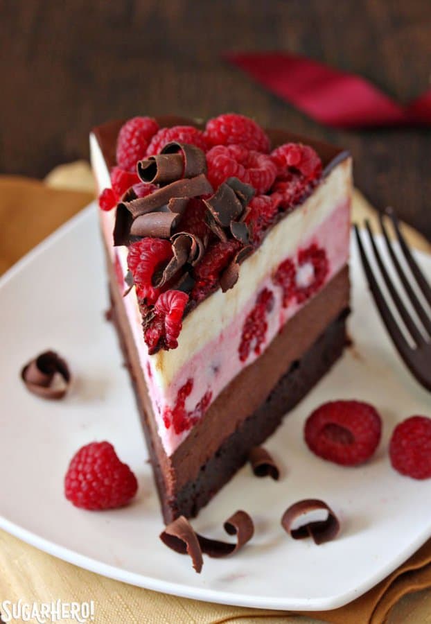 This cake has a moist, fudgy brownie base, three layers of light mousse—chocolate, raspberry, and vanilla, and then a glossy topping of chocolate and a tangle of raspberries and chocolate curls on top.
