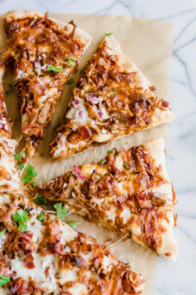Pulled Pork Pizza! Layers of bbq sauce, pulled pork, melty cheese, bacon bits and red onion. The perfect easy dinner recipe that puts your leftovers to work for you! Or use a quick shortcut by getting pulled pork from the market. Perfect Quick and easy family dinner!