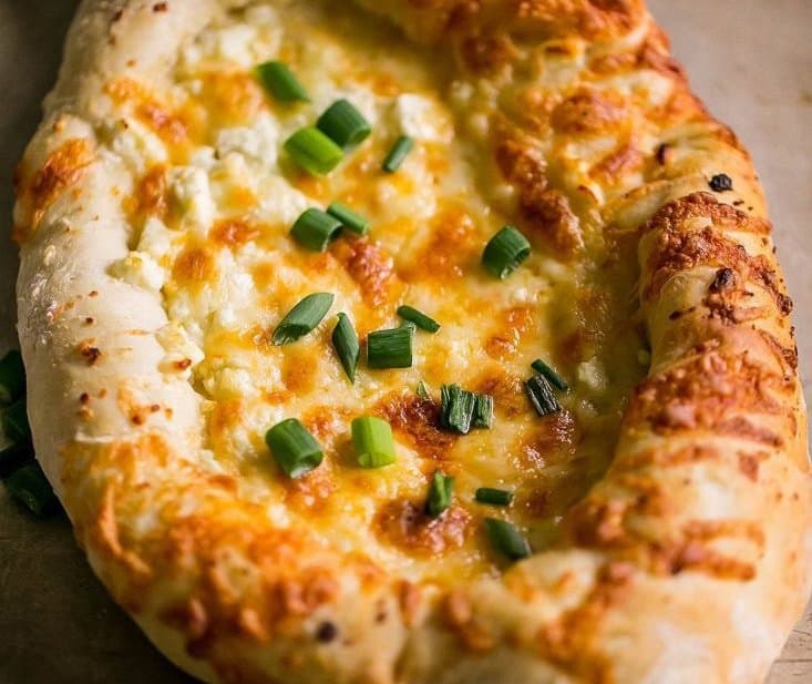Khachapuri, a traditional Georgian cheese bread rich with history from the Caucasus region, is a decadent and delicious rich appetizer.