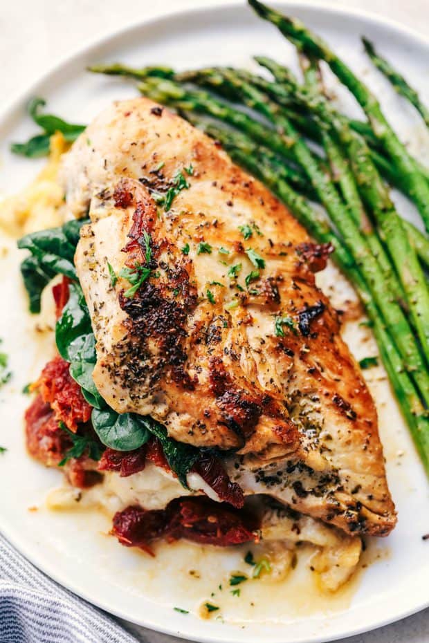Stuffed Tuscan Garlic Chicken are tender and juicy chicken stuffed with mozzarella cheese, sun-dried tomatoes, and spinach that gets baked in a creamy garlic sauce.  This meal will blow the family away!