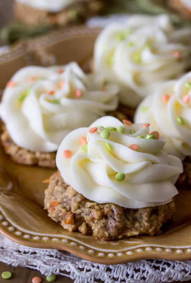 These carrot cake cookies are moist, oatmeal-based cookies that come together in a flash.  They are topped with a generous topping of signature sweet cream cheese frosting (and sprinkles, if you’re feeling festive).  These bite-sized treats are much simpler than making a whole cake!