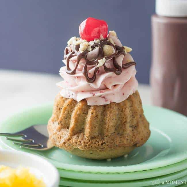 Banana Split Mini Bundt Cakes are such a Fun Treat!  Moist Banana Cake is Filled with Pineapple, and Topped with Strawberry Buttercream, Chocolate Sauce, Peanuts, and a Cherry on Top.  Perfect for your next Party!