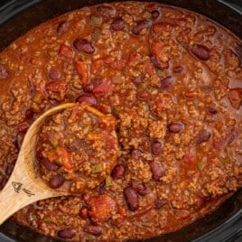 Crockpot chili made with ground beef, kidney beans, tomatoes, and peppers cooking in a slow cooker with a wooden spoon.
