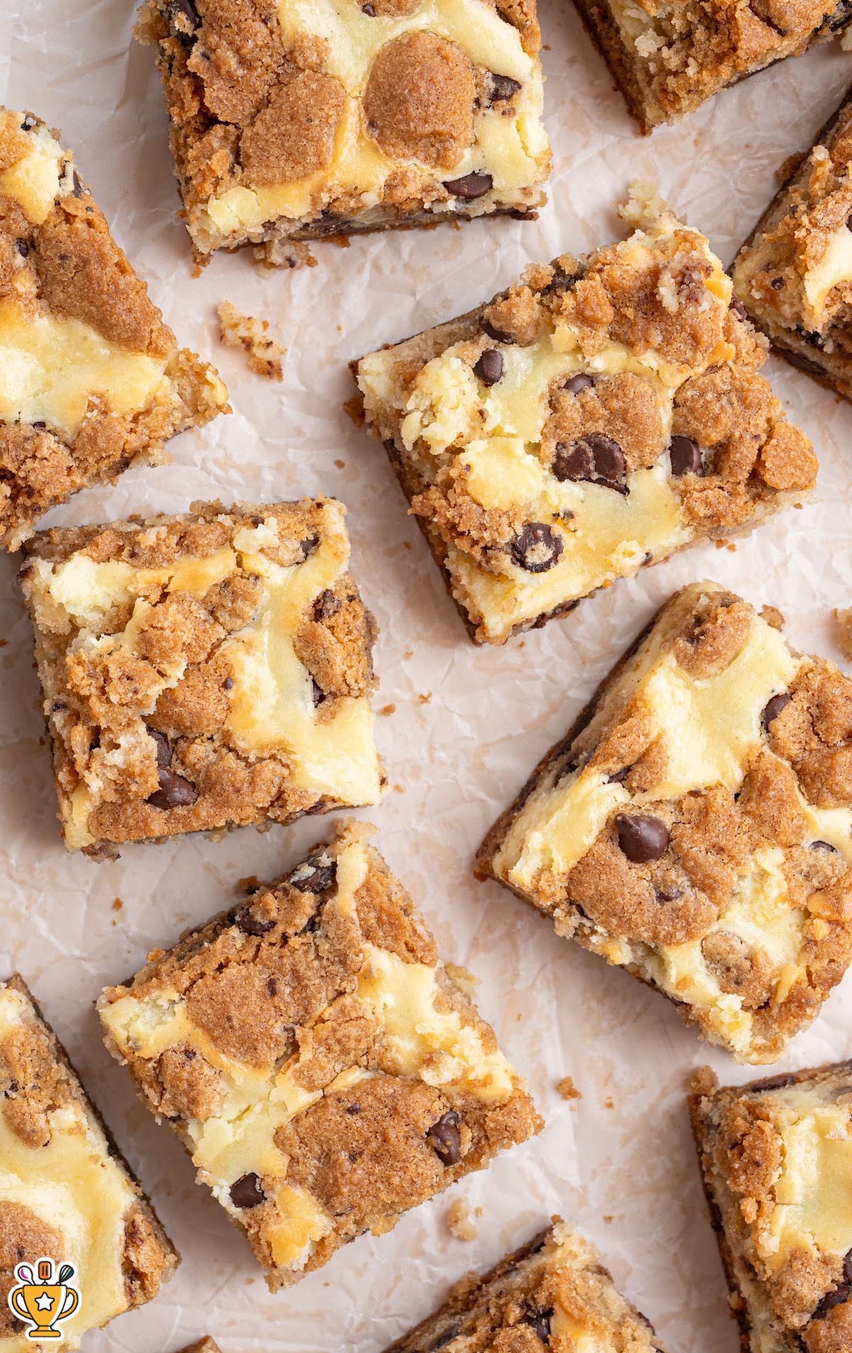 Flat lay of multiple chocolate chip cheesecake bars arranged on parchment paper, showing the golden brown cookie pieces and swirled cheesecake tops.