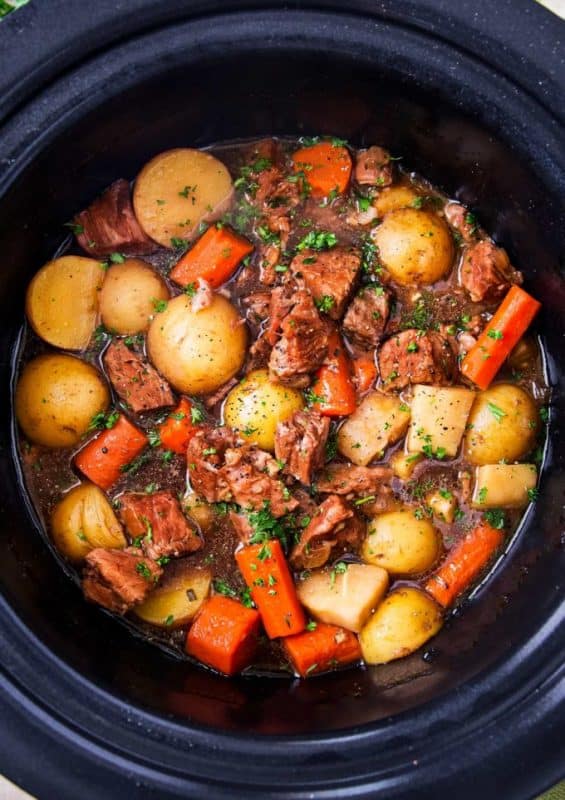 A pan filled with meat and vegetables cooking on a stove, with Beef and Slow Cooker