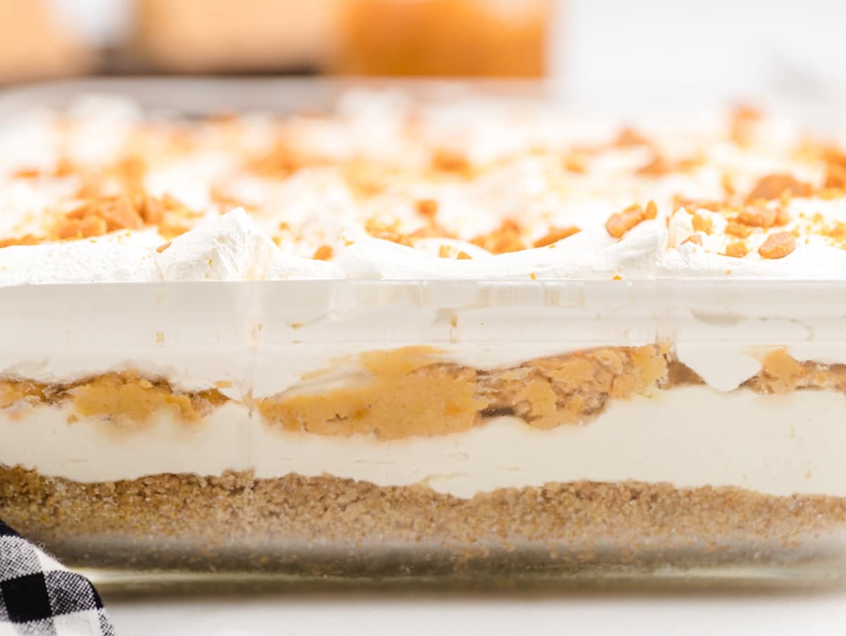 Side view of Butterscotch Delight through the glass dish, showing four layers: graham cracker crust, cream cheese, butterscotch pudding, and whipped topping.