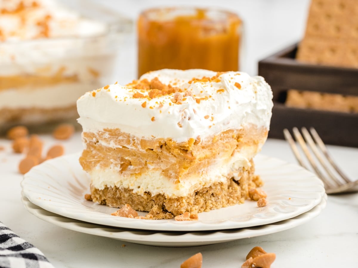 Slice of Butterscotch Delight on a white plate, with a jar of butterscotch sauce and graham crackers in the background.