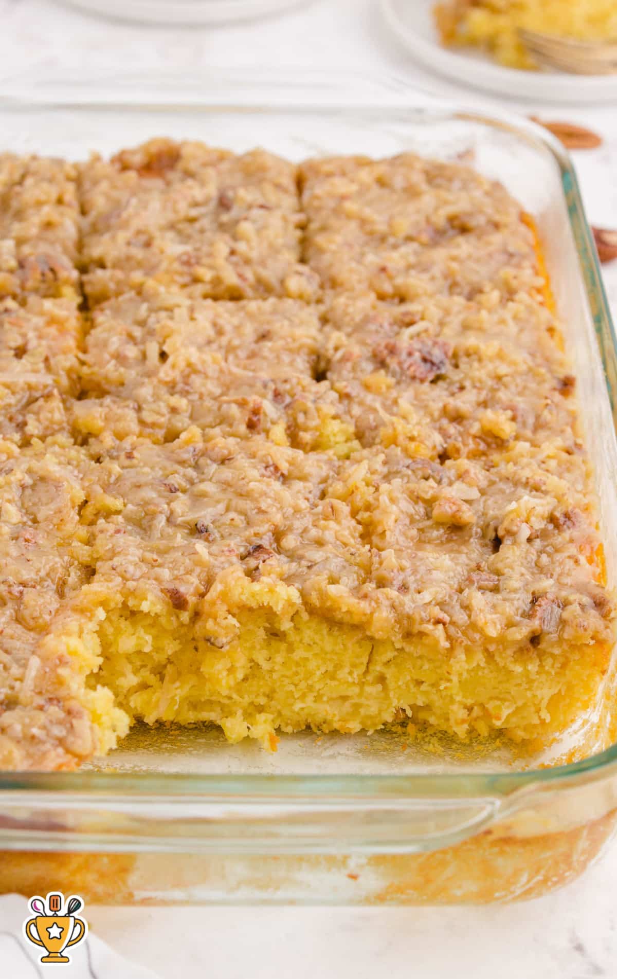 A freshly baked Southern-style tornado cake cut into squares and served in a glass baking dish, showing its moist yellow crumb and rich coconut-pecan topping.