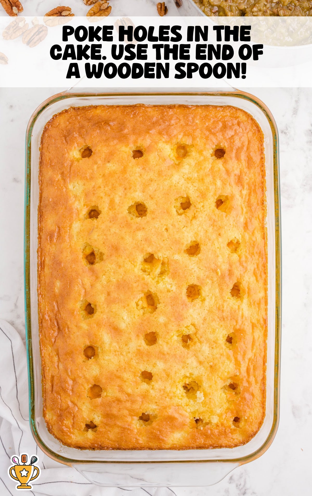 Baked yellow cake in a glass dish with evenly spaced holes poked across the surface using the handle of a wooden spoon, ready for topping.