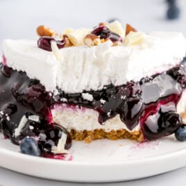 close up shot of a slice of blueberry delight topped with pecans and white chocolate curls on a plate