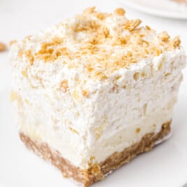 A slice of pineapple delight cake on a white plate with scattered crumbs nearby.