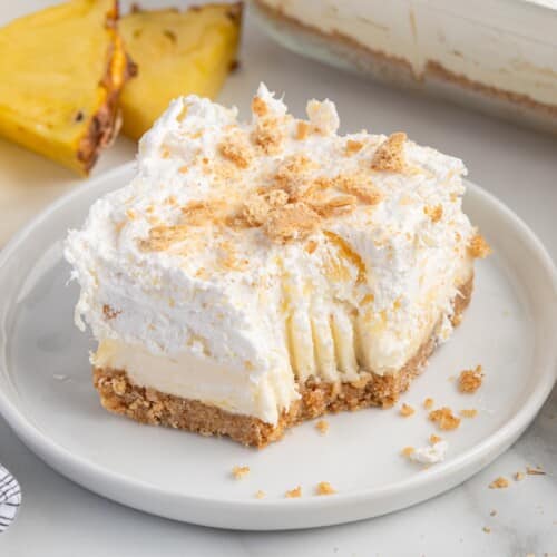 Partially eaten slice of pineapple delight with fluffy pineapple topping, cream cheese filling, and graham cracker crust.