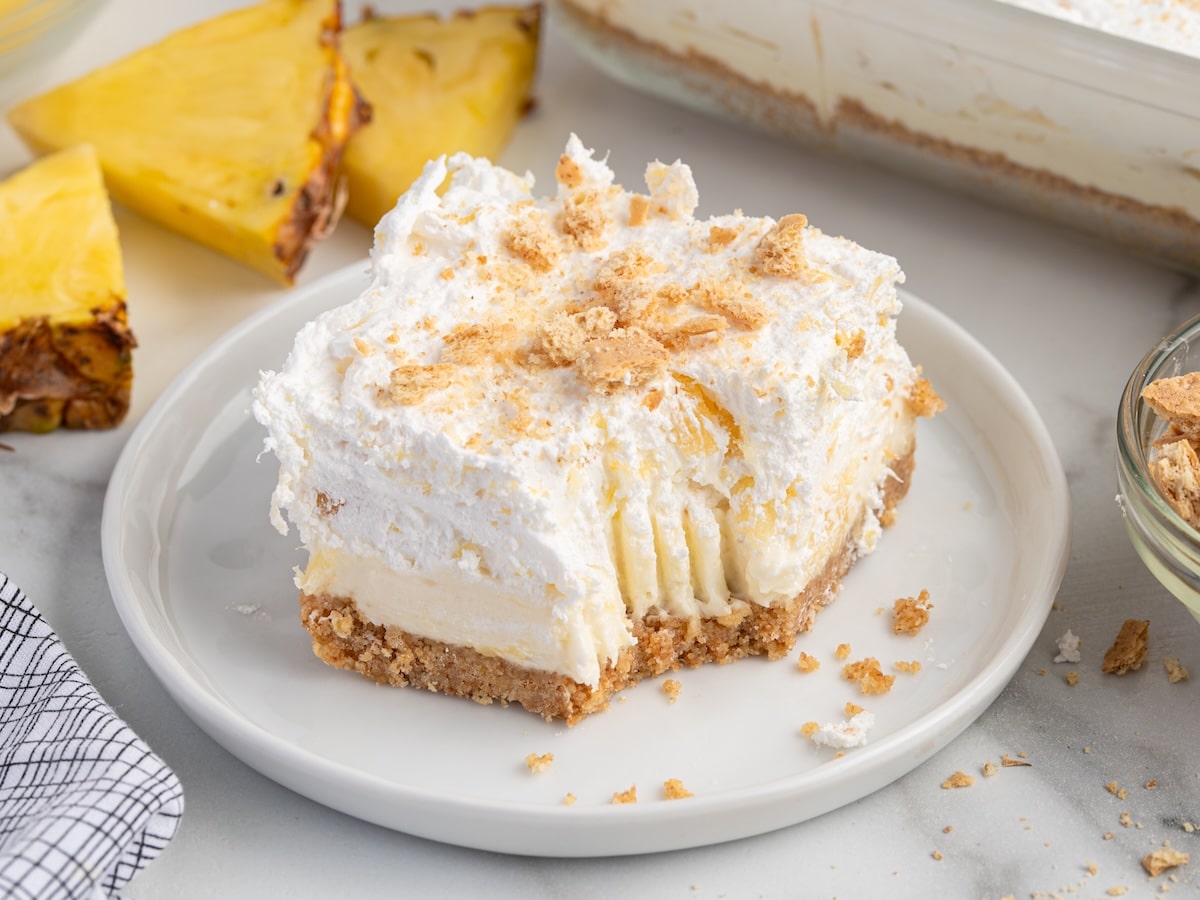 Partially eaten slice of pineapple delight with fluffy pineapple topping, cream cheese filling, and graham cracker crust.