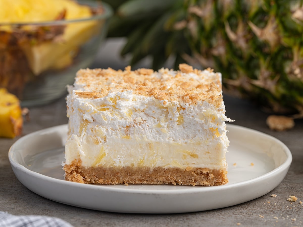 Square of pineapple delight on a plate with creamy pineapple layers, graham cracker crust, and crumb topping.