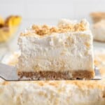 Slice of pineapple delight on a spatula showing layers of graham cracker crust, creamy pineapple filling, and whipped topping.