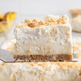 Slice of pineapple delight on a spatula showing layers of graham cracker crust, creamy pineapple filling, and whipped topping.