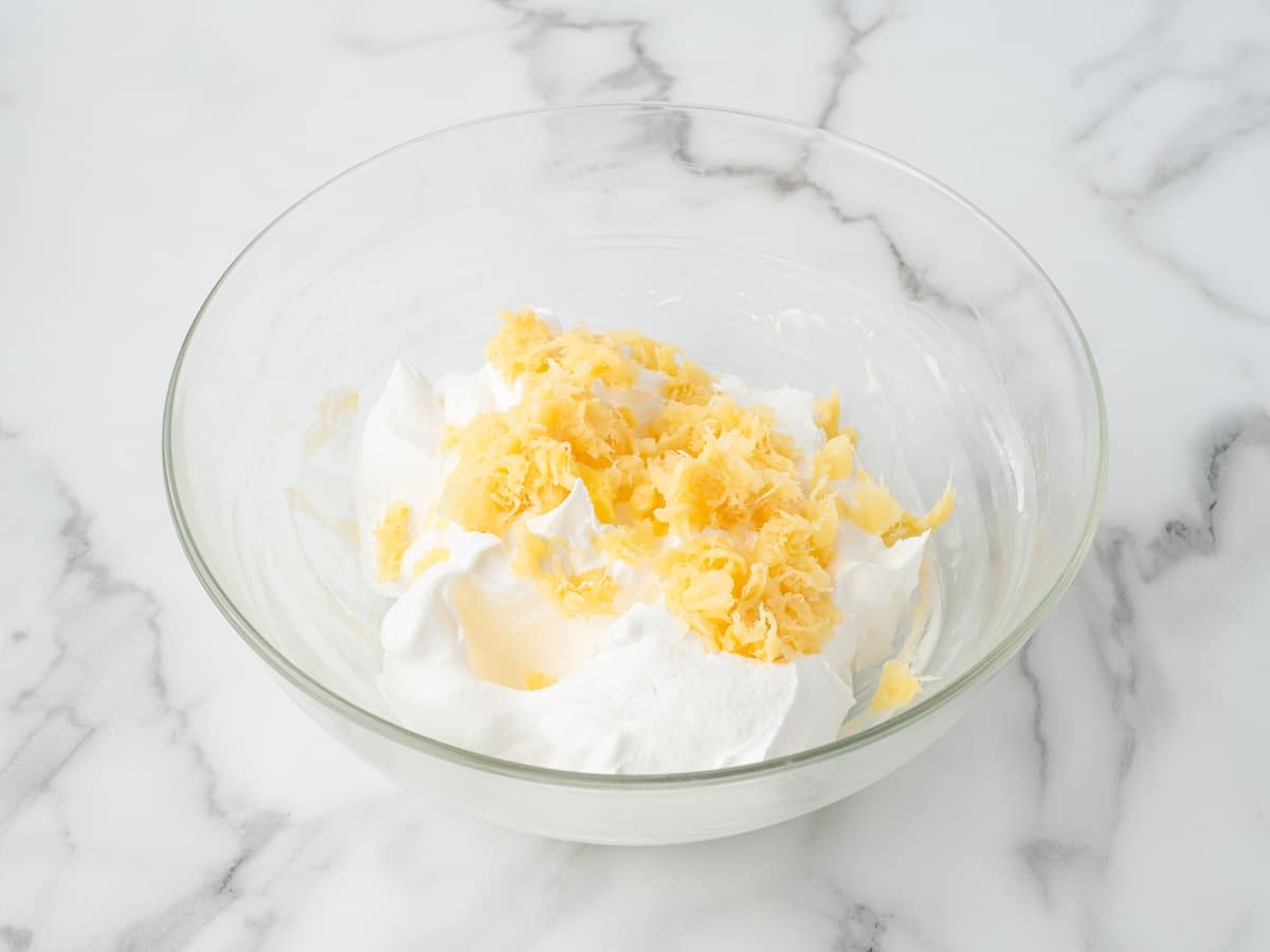 Crushed pineapple and whipped topping in a glass bowl ready to be combined.