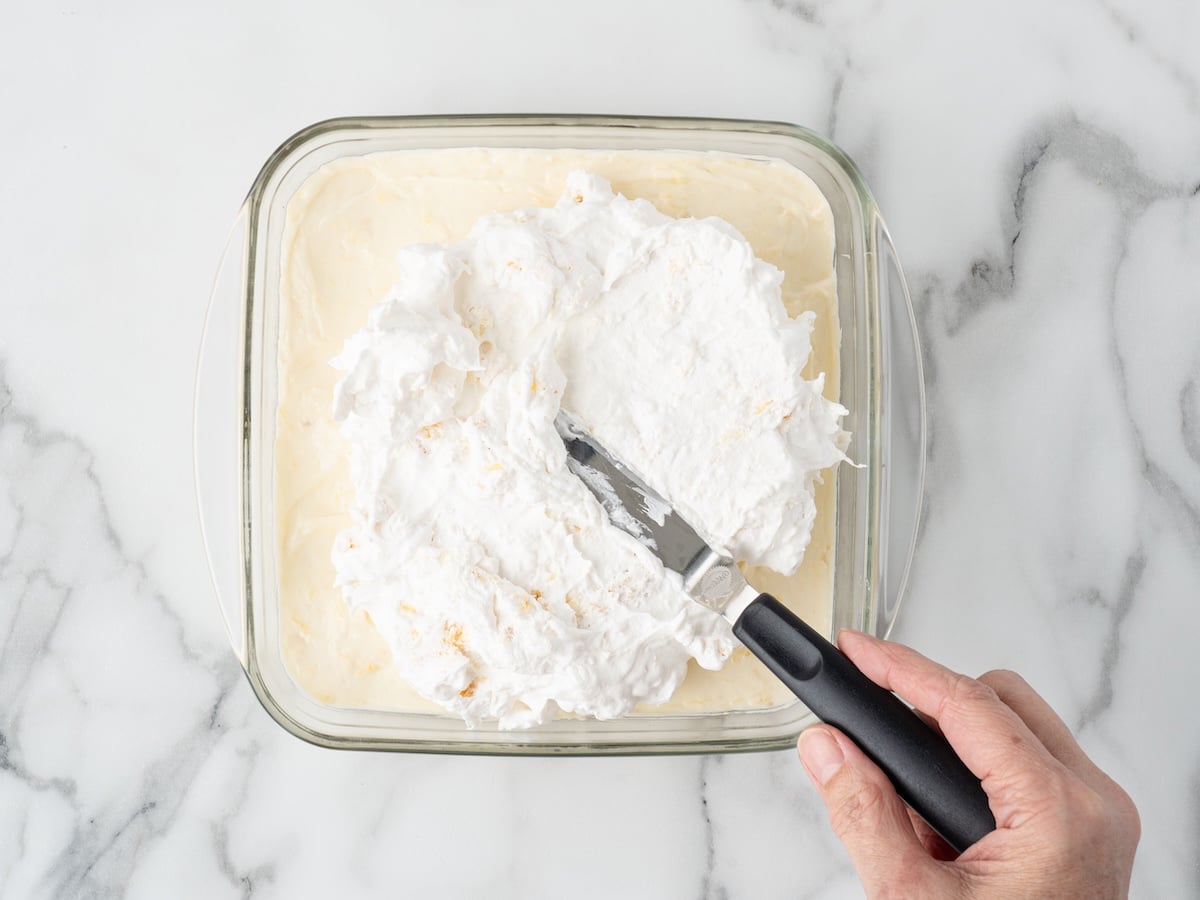 Pineapple whipped topping being spread over the cream cheese layer of pineapple delight.