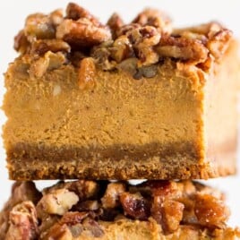 Stack of pumpkin cheesecake bars with crunchy pecan topping and thick gingersnap crust, highlighting creamy pumpkin filling and fall dessert layers.