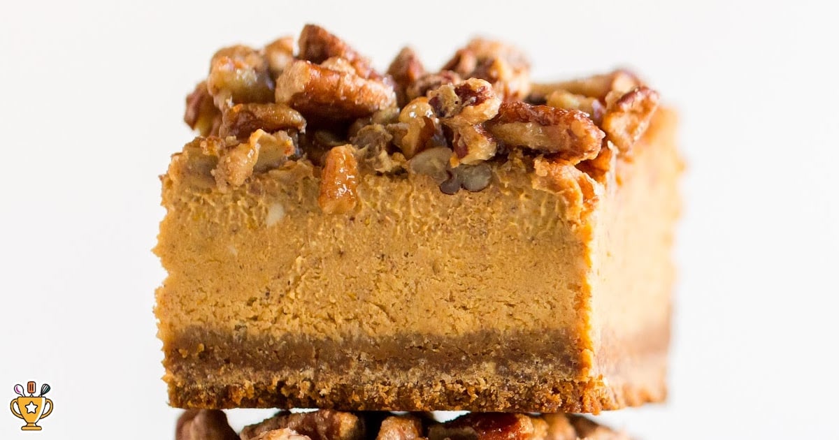 Detailed close-up of pumpkin cheesecake bar with crunchy candied pecans, creamy pumpkin spice cheesecake filling, and golden brown gingersnap crust.
