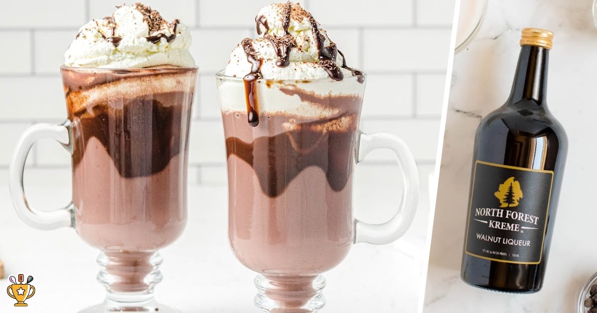 Two glass mugs of spiked hot chocolate with whipped cream and chocolate drizzle beside a bottle of walnut liqueur, showing the perfect holiday drink idea.