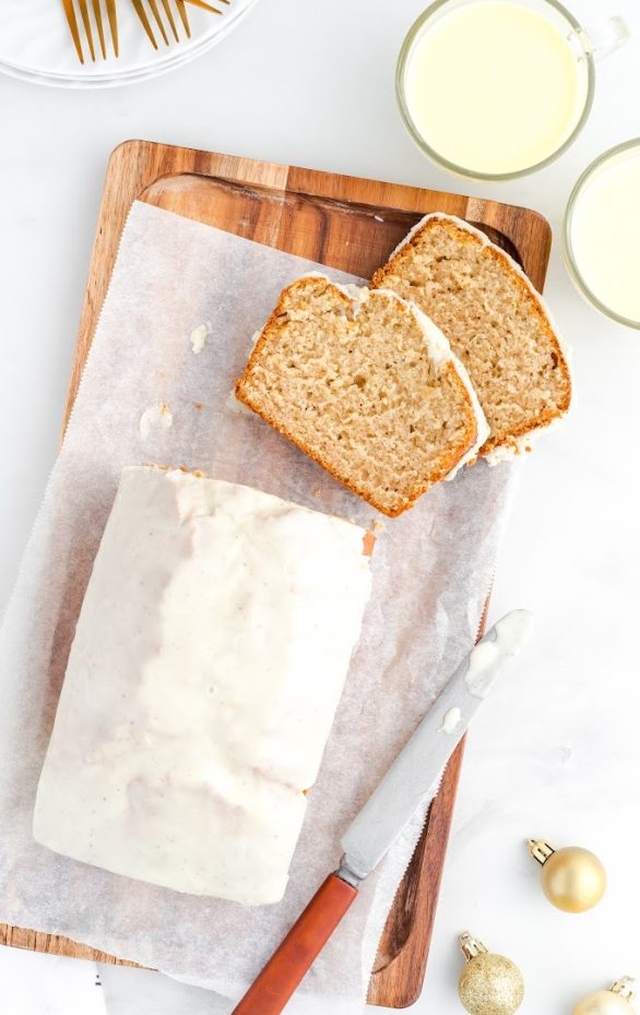 A piece of bread on a cutting board with a cake on a plate, with Eggnog