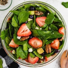 A bowl of salad on a plate, with Spinach and Strawberry