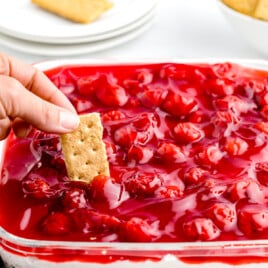 Cherry Cheesecake Dip with a person scooping up some with a graham cracker.