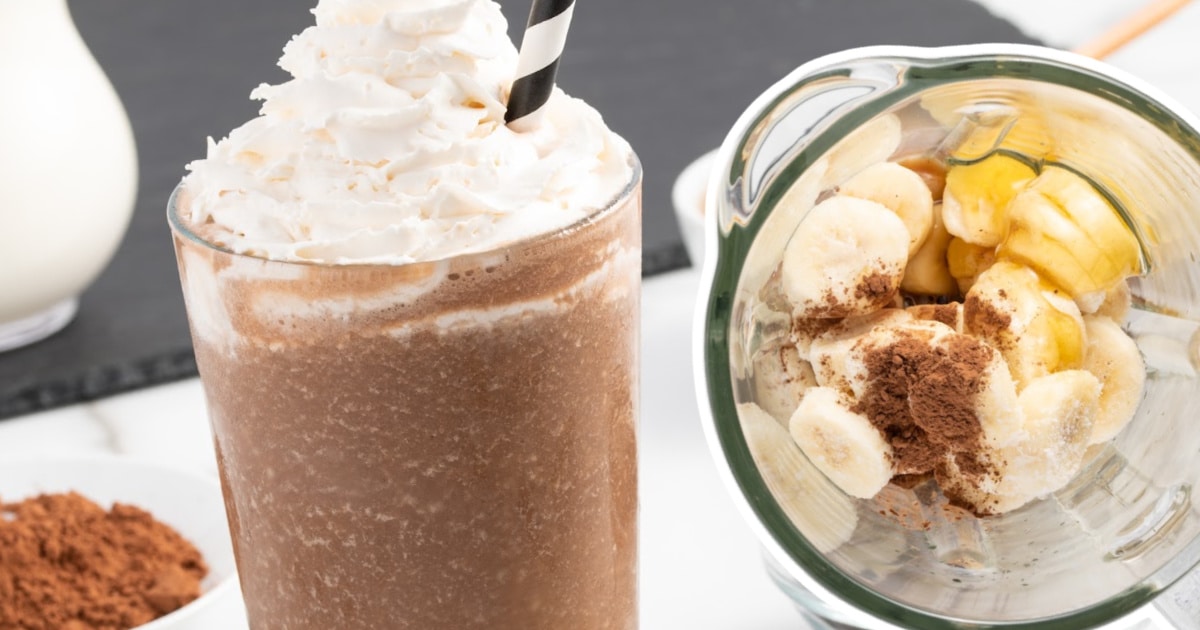 A glass full of coffee smoothie, next to a blender full of ingredients.