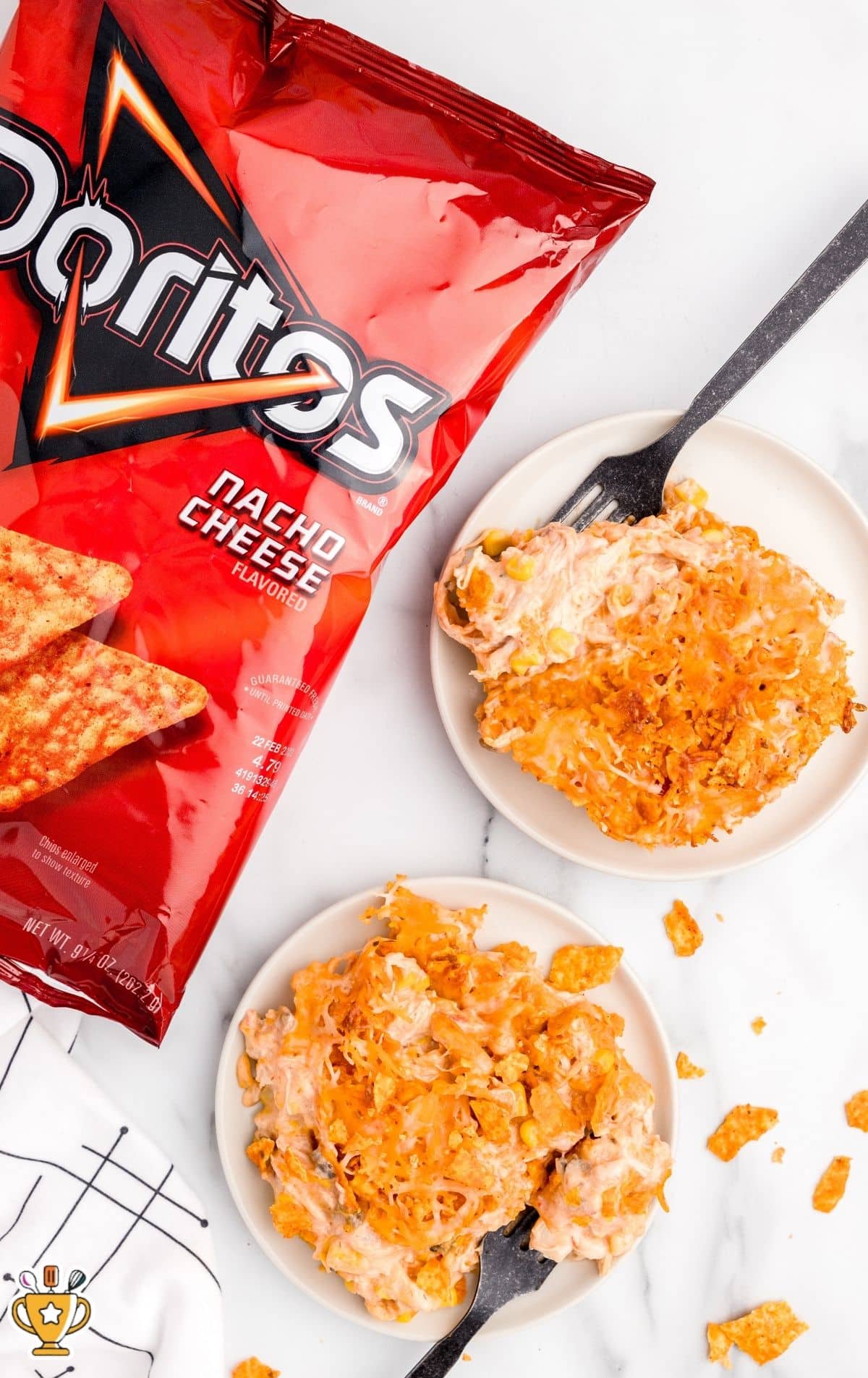 Overhead view of cheesy chicken Doritos casserole served on small plates with crushed nacho cheese chips and melted cheese on a white marble countertop.