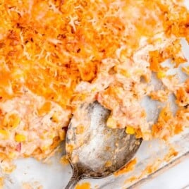 Spoon scooping a creamy, cheesy Doritos chicken casserole from a glass baking dish, showing layers of chicken, corn, and crushed chips.