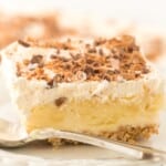 Close-up of a thick, creamy slice of butter pecan crunch no-bake dessert on a plate, showing the graham cracker crust, pudding layer, and whipped topping with crunchy toffee pecans.