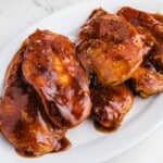 Close-up of four juicy Coca Cola chicken breasts coated in thick, glossy sauce, served on a white oval platter.
