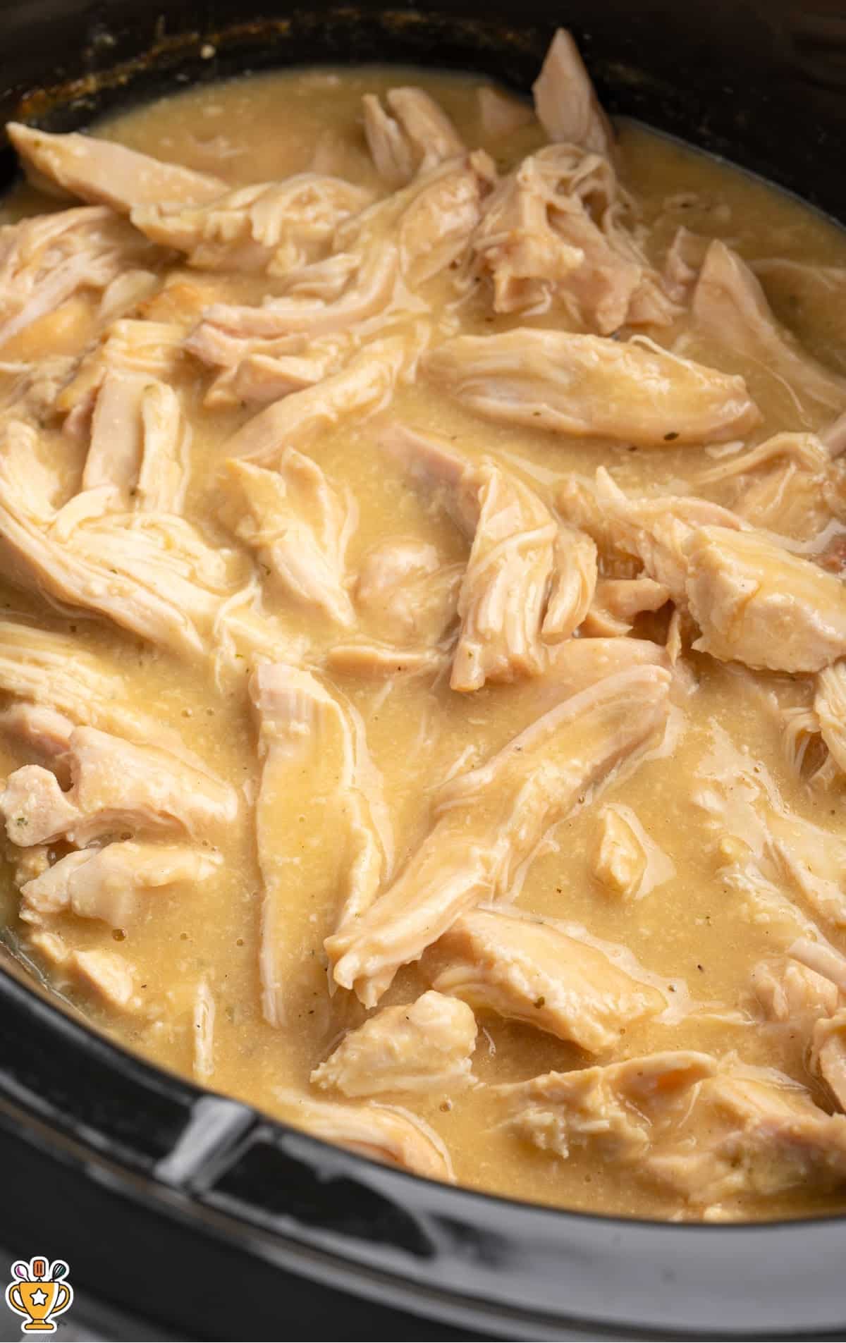 Crockpot filled with creamy chicken and gravy, with a metal ladle full of tender shredded chicken held above the slow cooker.
