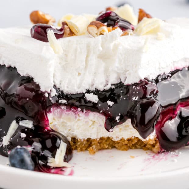 close up shot of a slice of blueberry delight topped with pecans and white chocolate curls on a plate