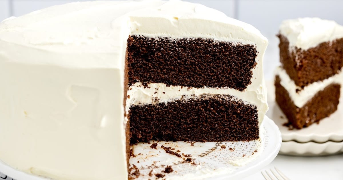 a close up shot of Chocolate Cake with Whipped Cream Frosting on a cake stand with a couple of slices taken out