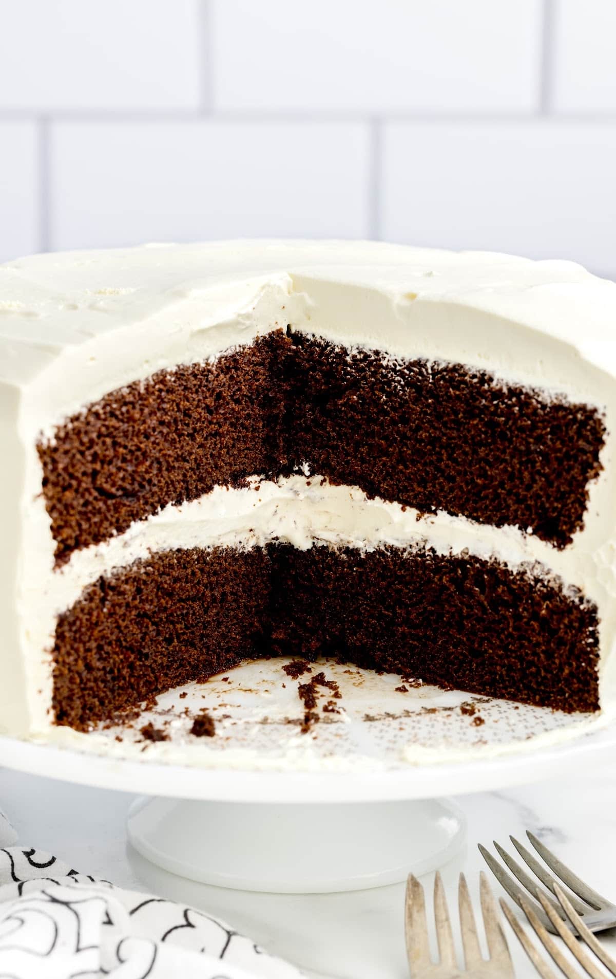 a close up shot of Chocolate Cake with Whipped Cream Frosting on a cake stand with a couple of slices taken out