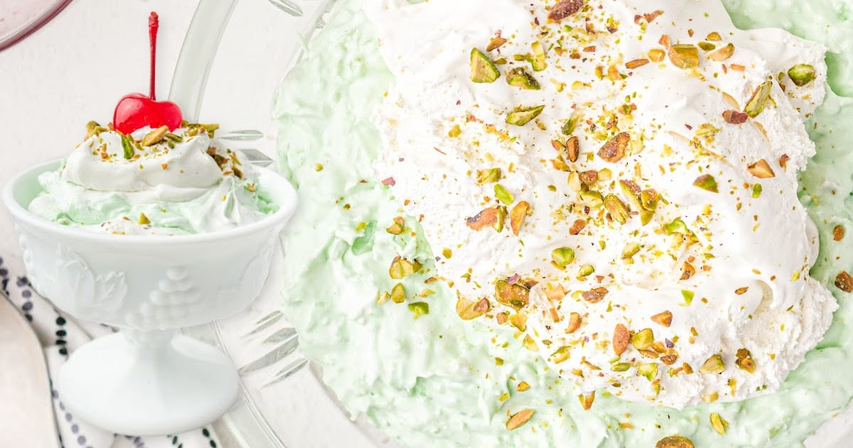 close up shot of a large bowl of pistachio salad topped with whipped cream and crushed pistachios
