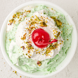 close up shot of a small bowl of pistachio salad topped with whipped cream and crushed pistachios