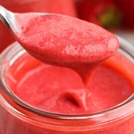 a close up shot of Strawberry Curd in a glass cup with a spoon grabbing a piece