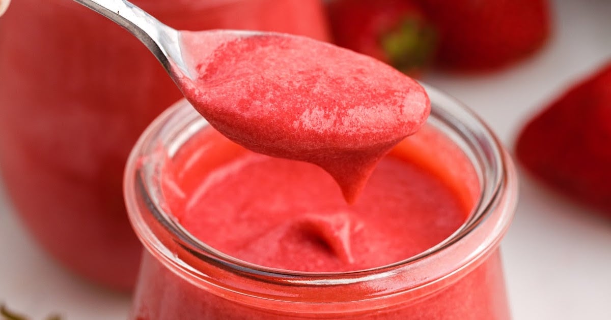 Strawberry Curd in a glass cup with a spoon grabbing a spoonful