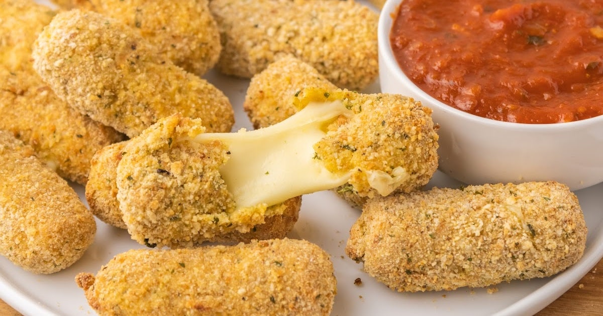 a close up shot of Air Fryer Mozzarella Sticks on a plate with one being pulled apart"