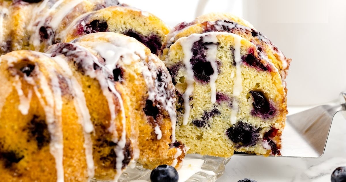 close up shot of a loaf of pound cake topped with glaze and blueberries