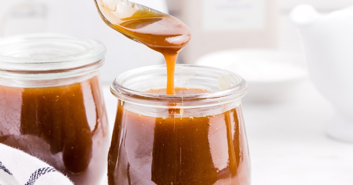 close up shot of Caramel Sauce in a jar with a spoonful of sauce being scooped out of the jar