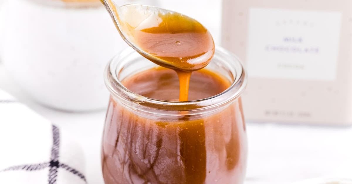 close up shot of Caramel Sauce in a jar with a spoonful of sauce being scooped out of the jar