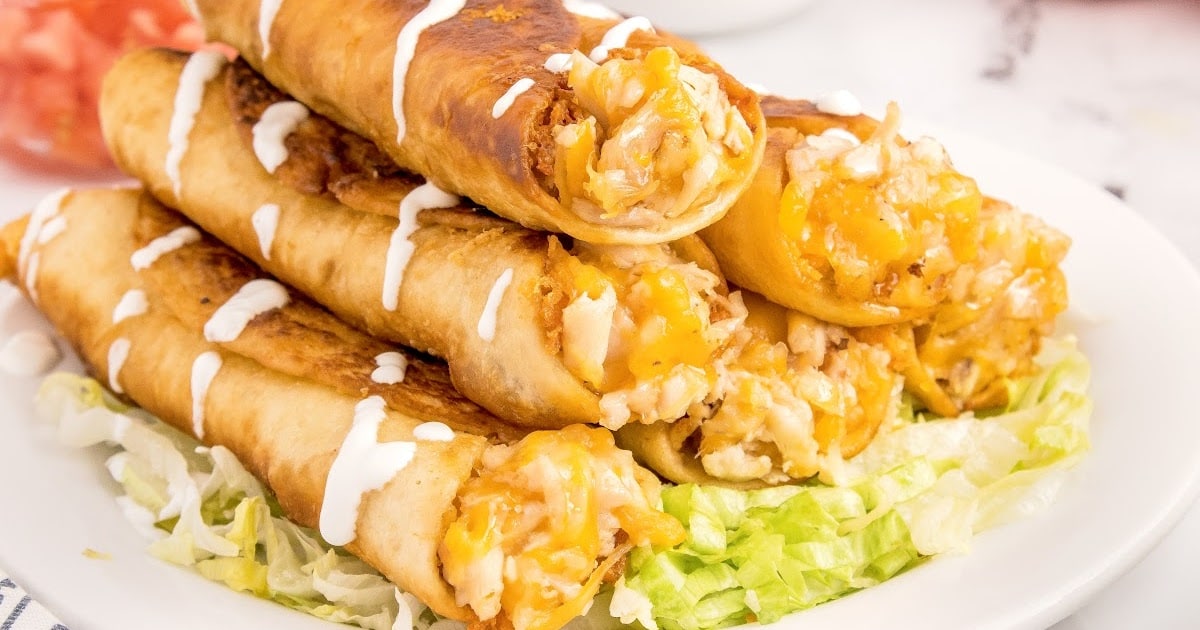 overhead shot of a plate of Chicken Flautas topped on a bead of avocado and garnished with toppings