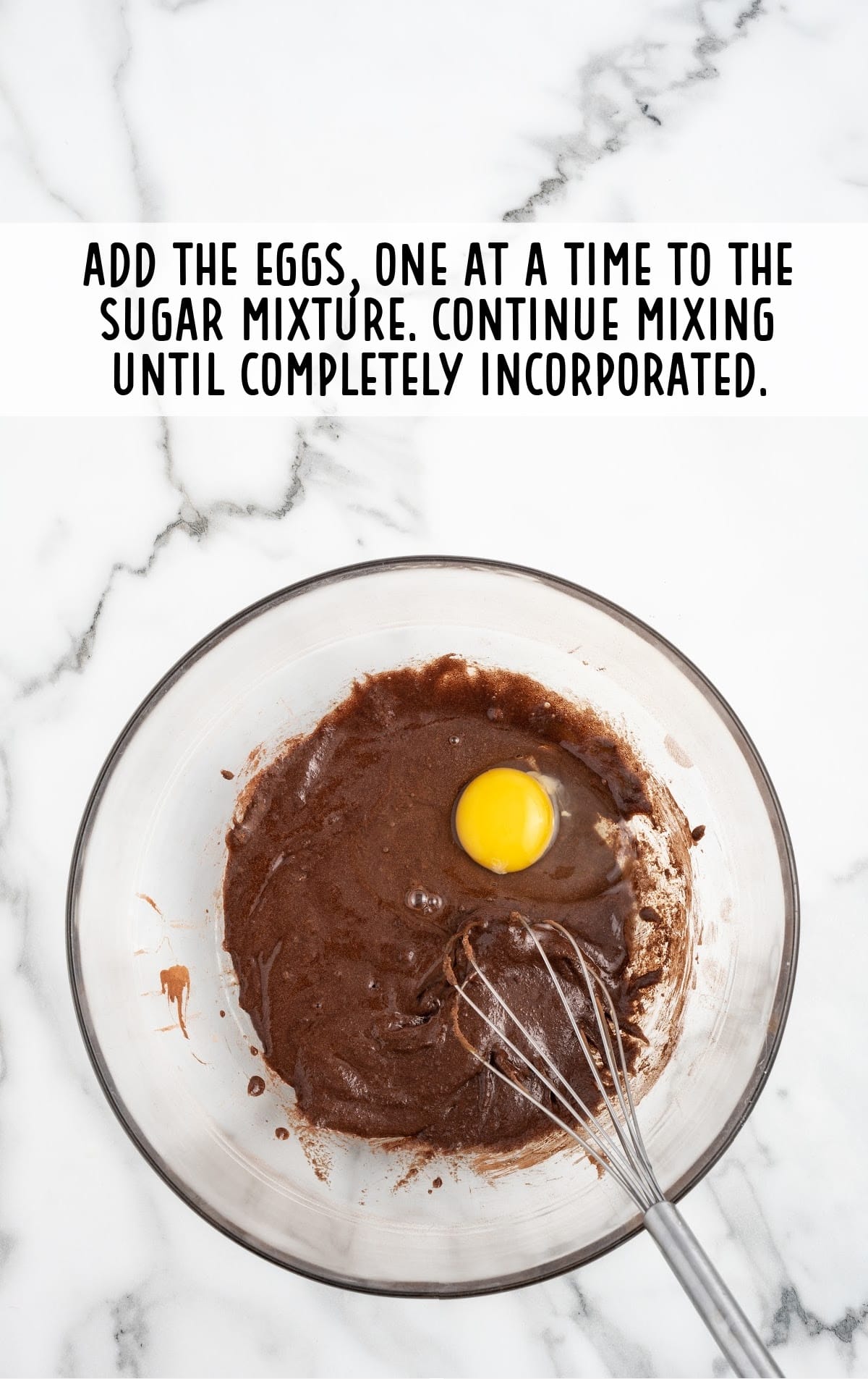 eggs added in sugar and cocoa mixture in a clear bowl with a whisker