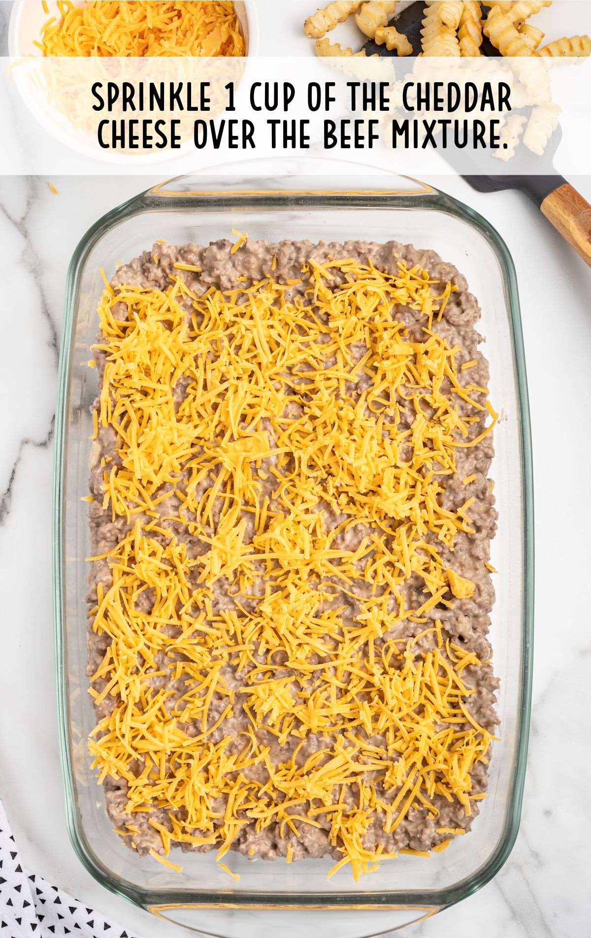 cheddar cheese sprinkled over the beef mixture in a baking dish